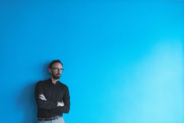 Thoughtful male executive standing against blue wall in office