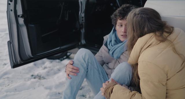 Elsa Steixner and Lennart König sitting on the ground next to a parked car