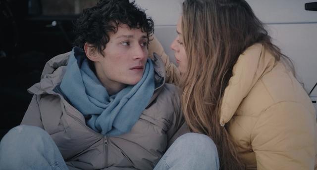 Elsa Steixner singing to Lennart König sitting on the ground next to a parked car